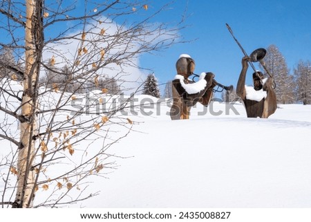 Two wooden sculptures with brass musical instruments (trumpet and trombone) in the snow.