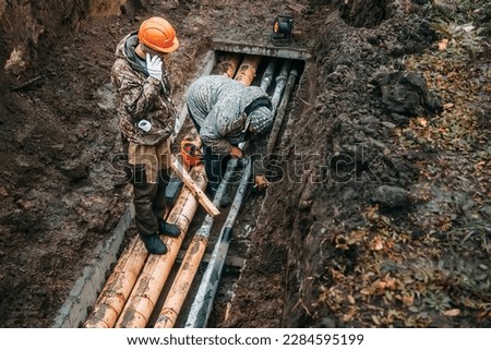 Two workers change public water pipes in trench on rainy autumn day. Troubleshooting. Breakthrough of water pipeline underground. Utilities. Real workflow..