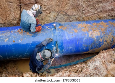 Two workers are connecting underground sewers at a construction site to repair the water pipes by welding.