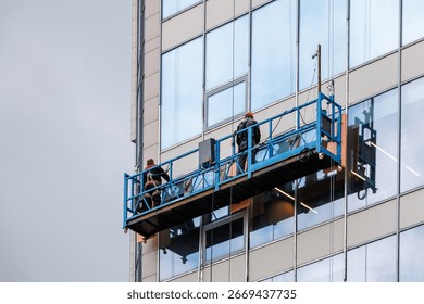 Two workers in a construction cradle are working at altitude. Installation work on the wall of a skyscraper