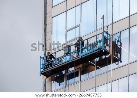 Two workers in a construction cradle are working at altitude. Installation work on the wall of a skyscraper