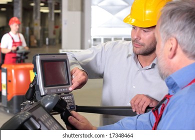 two workers with control panel in factory, third one on forklift in background - Powered by Shutterstock