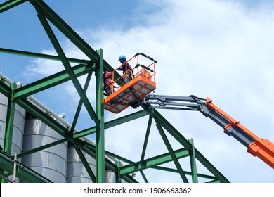 Two workers are driving the Orange articulate boom lift or telescopic boom lifts and bucket crane mounted on truck to safety for working at heights and articulating boom lift reaching high up.