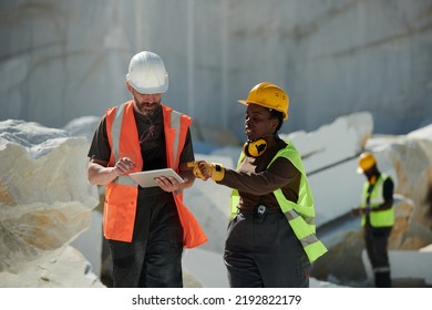 Two Workers Of Factory Situated On Territory Of Marble Quarry Discussing Online Manual Guide While Black Woman Pointing At Tablet Screen