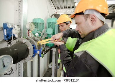 Two workers fixing pipes with manometer on high pressure system at factory