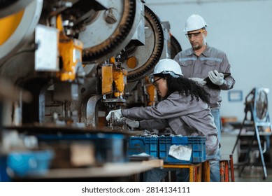 Two workers are focused on using machines in a factory. One worker checks parts while another stands by. The environment is busy with tools and equipment around them.