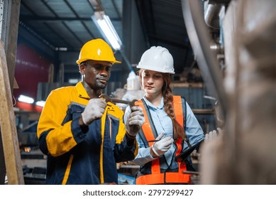 Two workers hold small objects closely. One wears yellow hard hat and blue,yellow work jacket. The other has white hard hat and orange safety vest
