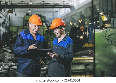 Two Workers At An Industrial Plant With A Tablet In Hand, Working Together Manufacturing Activities