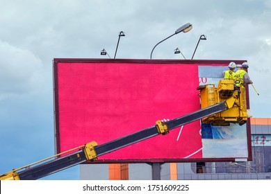 Two workers install red billboard on roadside of city street