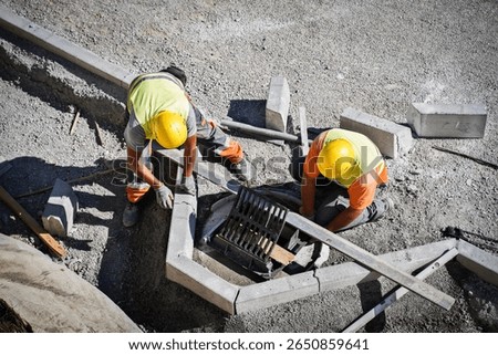 Two workers installing a drainage cover with an aluminum leveling bar on a highway construction site, ensuring perfect alignment