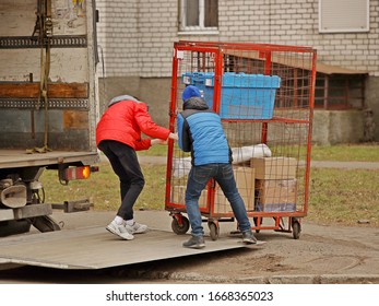 Two workers are loading a trolley with a cage for transporting goods onto the lift of a truck for transportation. Automation of manual work of loaders. Elevator platform on the rear side of the road 
