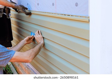 Two workers are measuring installing vinyl siding on house exterior under work day