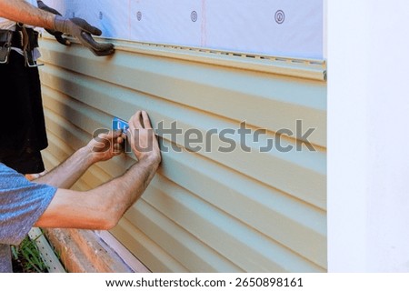 Two workers are measuring installing vinyl siding on house exterior under work day