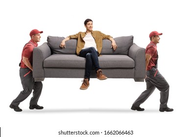 Two workers from a moving company carrying a sofa with a young man sitting isolated on white background