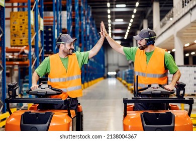 Two Workers On Forklifts. Giving High Five And Smiling At Each Other At Warehouse.