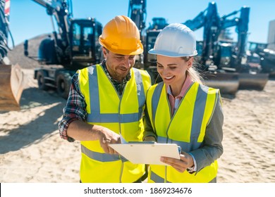 Two workers in open cast mine standing in front of heavy machinery with clipboard discussing