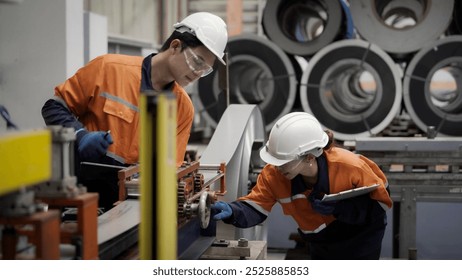 Two workers in orange and blue safety gear are inspecting a machine. Scene is serious and focused, as the workers are wearing hard hats and safety glasses to protect themselves while working - Powered by Shutterstock