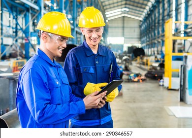 Two workers in production plant as team discussing, industrial scene in background - Powered by Shutterstock