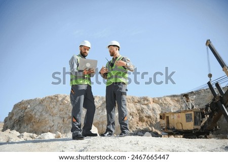 Two workers and quarry in background.