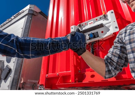 Two workers shake hands in front of a red shipping container, symbolizing collaboration in logistics.