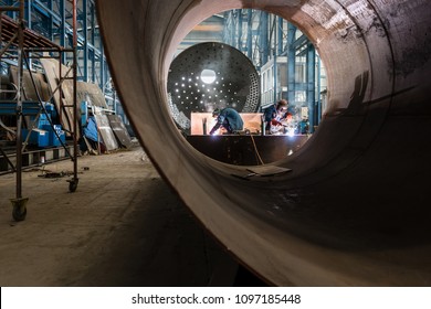 Two workers welding in the interior of a factory manufacturing metallic cylinders for industrial boilers 