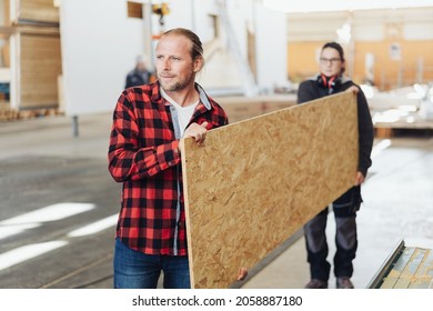 Two workers in a woodworking factory carrying a large sheet chipboard or particle board with focus to the man in front - Shutterstock ID 2058887180