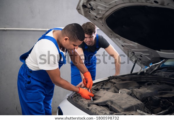Two workmen repair a\
damaged car engine