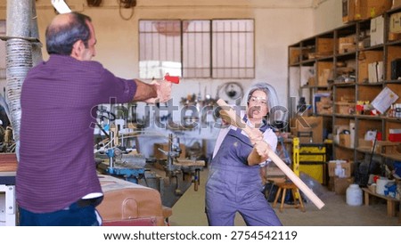 Two workshop workers playing, using a toy gun and a wood stick