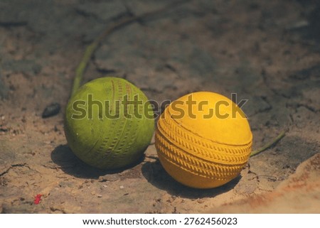 Two worn plastic cricket balls resting on the dusty soil in Birbhum West Bengal under direct daylight capturing directional shadows that highlight systemic poverty and economic crisis balanced by pure youthful resourcefulness for play and childhood concepts.
