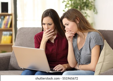 Two Worried Friends Watching Media Content On Line With A Pc Sitting On A Sofa In The Living Room In A House Indoor