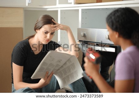 Two worried roommates assembling kitchen furniture checking installation manual reforming home