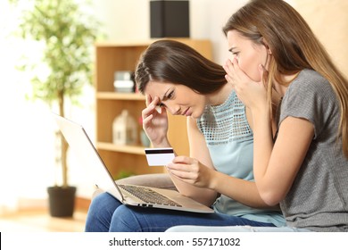 Two worried roommates having problems buying on line sitting on a couch in the living room in a house interior