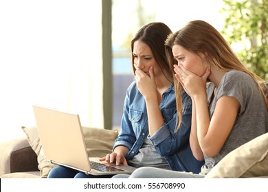 Two Worried Roommates Reading Bad News Or Inappropriate Content On Line With A Pc Sitting On A Couch In The Living Room In A House Interior