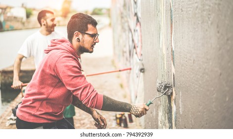 Two writers covering the wall with grey color before painting their picture - Contemporary artists at work - Urban lifestyle, street art and youth concept - Focus on right man face