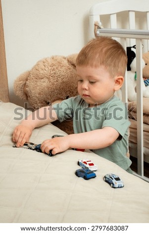 Two year old boy playing with small cars on bed. Racing and parking toy vehicles. Fine motor skills through push and go play. Classic boyish toy fun