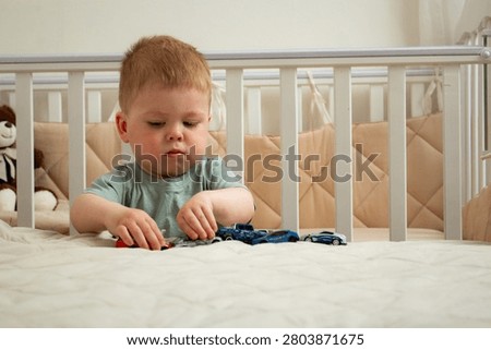 Two year old boy playing with small cars on bed. Racing and parking toy vehicles. Fine motor skills through push and go play. Classic boyish toy fun
