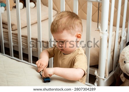 Two year old boy playing with small cars on bed. Racing and parking toy vehicles. Fine motor skills through push and go play. Classic boyish toy fun