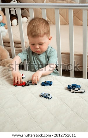 Two year old boy playing with small cars on bed. Racing and parking toy vehicles. Fine motor skills through push and go play. Classic boyish toy fun