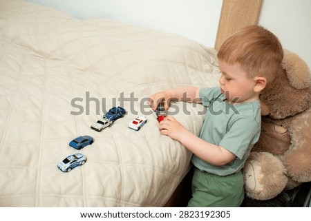 Two year old boy playing with small cars on bed. Racing and parking toy vehicles. Fine motor skills through push and go play. Classic boyish toy fun