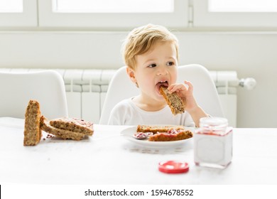 Two Year Old Toddler Boy Eating Jam And Bread By Himself, Sitting In All White Environment Wearing White Clothes