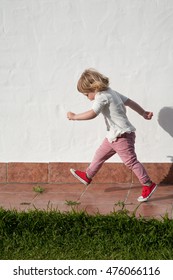 Two Years Old Blonde Child Profile Walking Active On Tiled Sidewalk At Garden