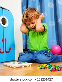 Two years old boy playing and laughing sitting on the floor in his room with mosaic