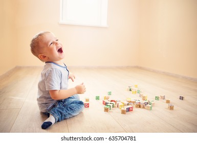 Two Years Old Child Sitting On The Floor. Pretty Little Boy Palying With Wooden Cubes At Home