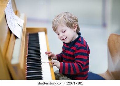 Two years old happy toddler boy playing piano at music school