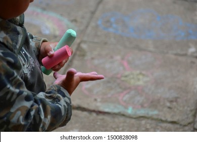 Two years old toddler - a boy - is holding pink and green chalks in his dirty hands. Small child is playing outside with chalks. Little kid is sketching on a pavement. - Shutterstock ID 1500828098