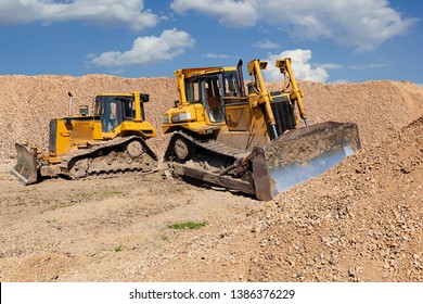 Two yellow dozers on a dirt terrain with blue sky with clouds in the background