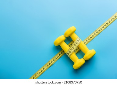 two yellow dumbbells and a measuring tape on a blue background with copy space.