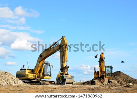 Two yellow excavators at a construction site. Excavator with crusher bucket for crushing concrete. Construction waste recycling for construction mix. Sifting, grinding and separation of concrete 