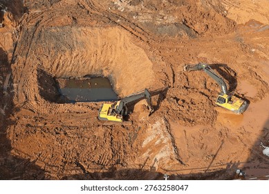 Two yellow excavators digging in deep muddy pits at a large construction site. Concept of industrial excavation.
