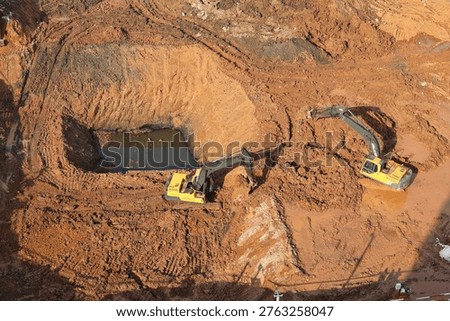 Two yellow excavators digging in deep muddy pits at a large construction site. Concept of industrial excavation.
